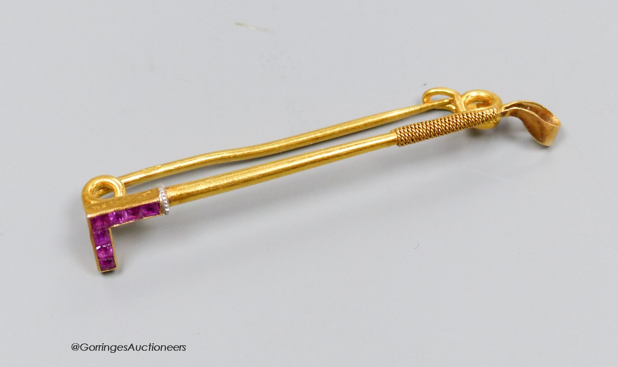 A Lacloche Freres gold and ruby riding whip brooch, signed, gross 3g, 5cm. In original box.